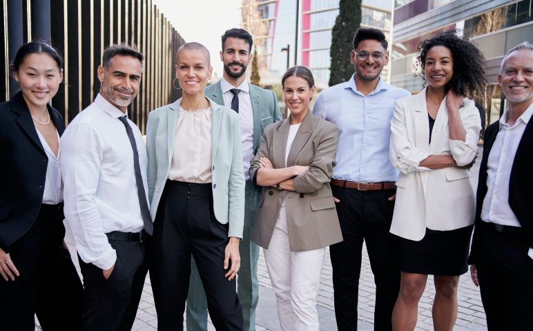 Team portrait multi-ethnic professionals smiling posing with confidence. Young and mature colleagues Team portrait multi-ethnic professionals smiling posing with confidence. Young and mature colleagues looking at camera cheerful expression. Group of office workers outside a startup business company.